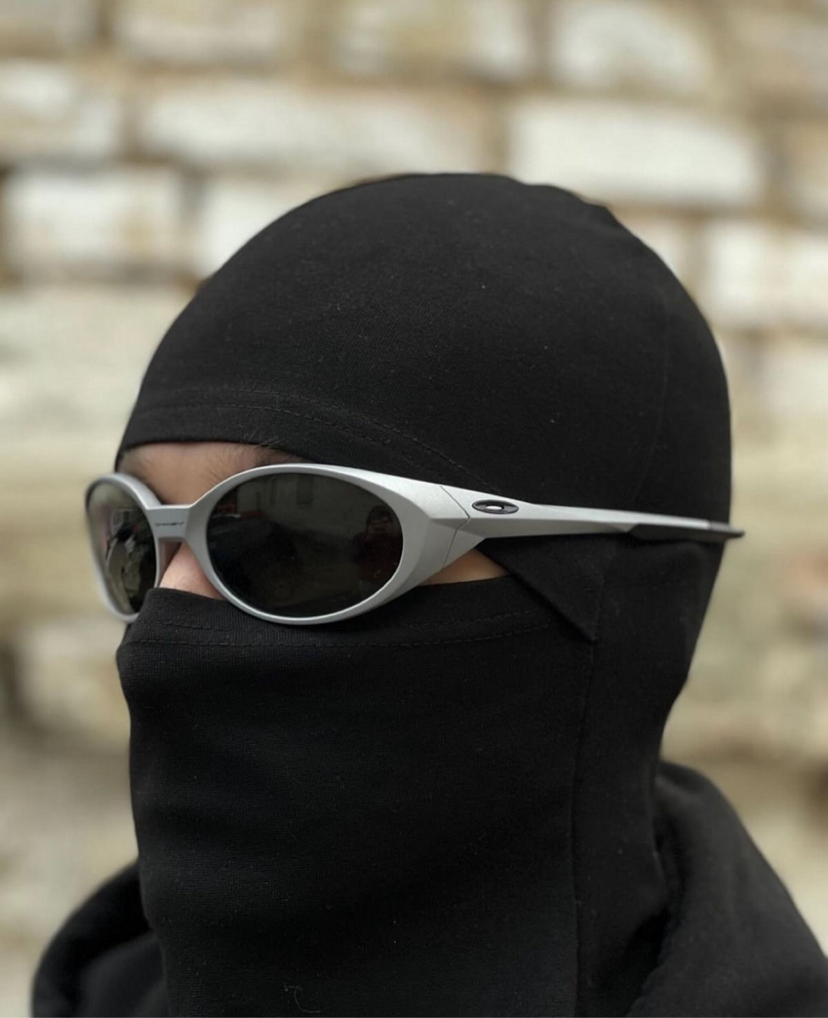 Silver oval sunglasses worn with a black balaclava, seen in profile